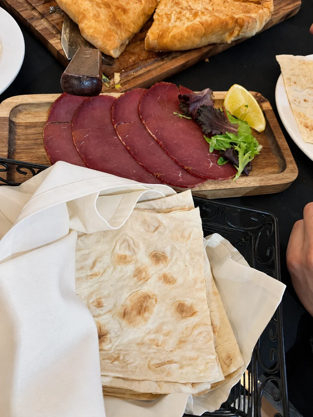 Thin slices of Armenian basturma on a wooden board beside lavash bread