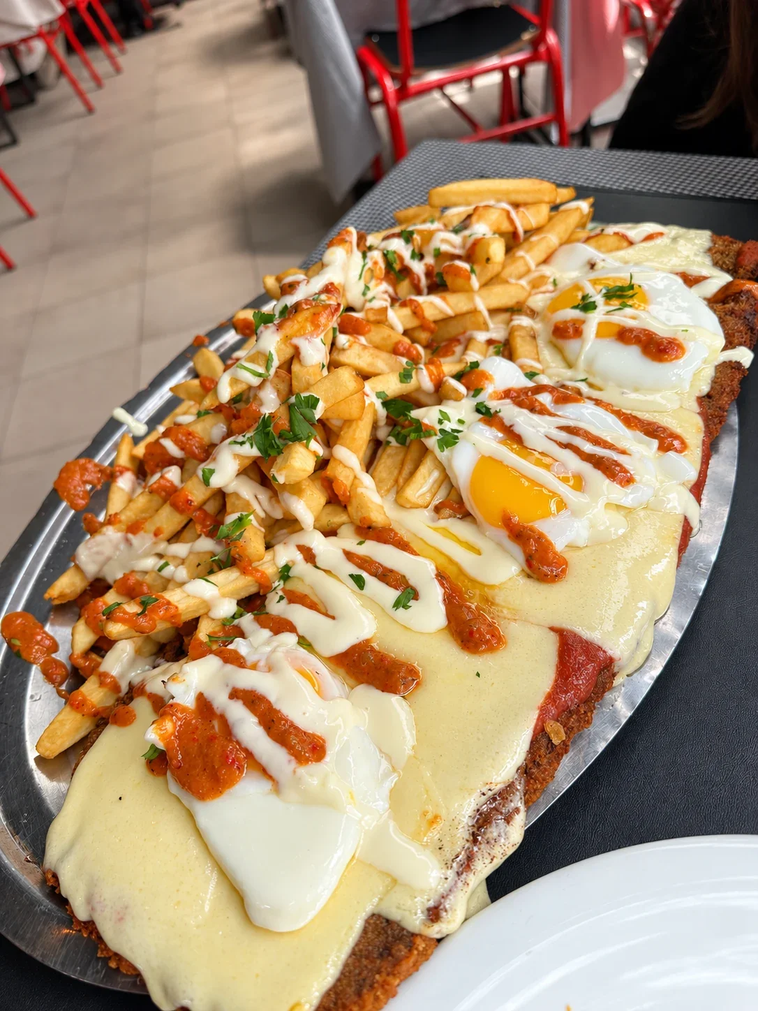 A Gran Bodegón milanesa covered with melted cheese, fried eggs and sauces, with fries alongside