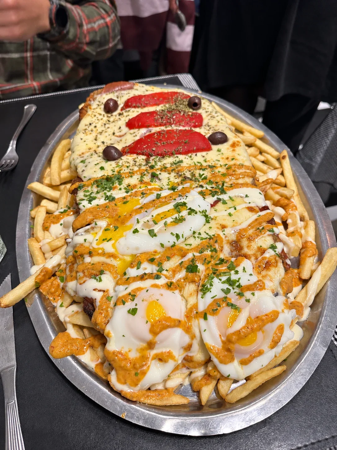A Milagrosa milanesa with fried eggs and sauces on one half and ham, peppers and olives on the other