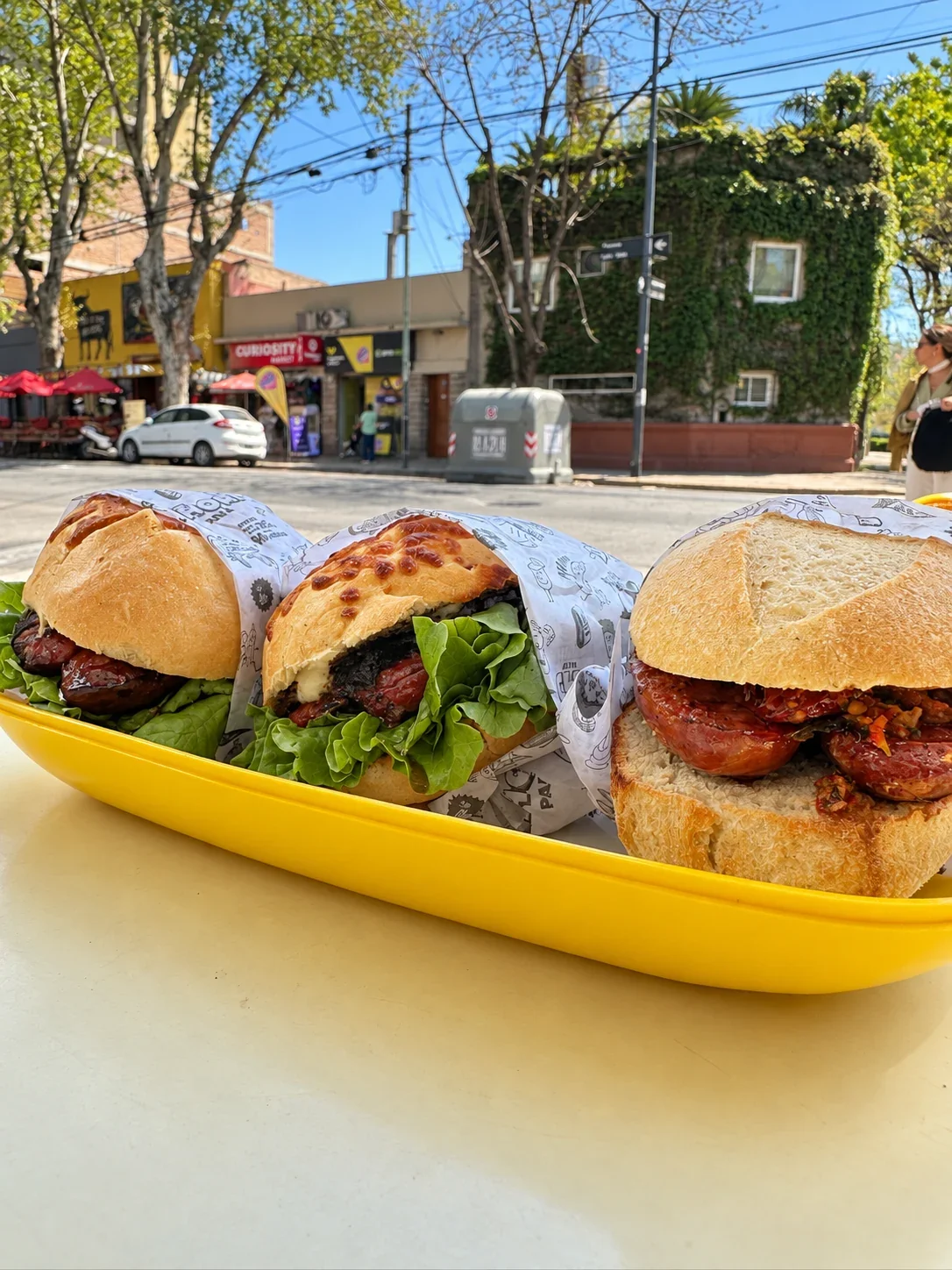 Two smoked-pork sandwiches in cheese bread and a Chori de Cancha on an outdoor table