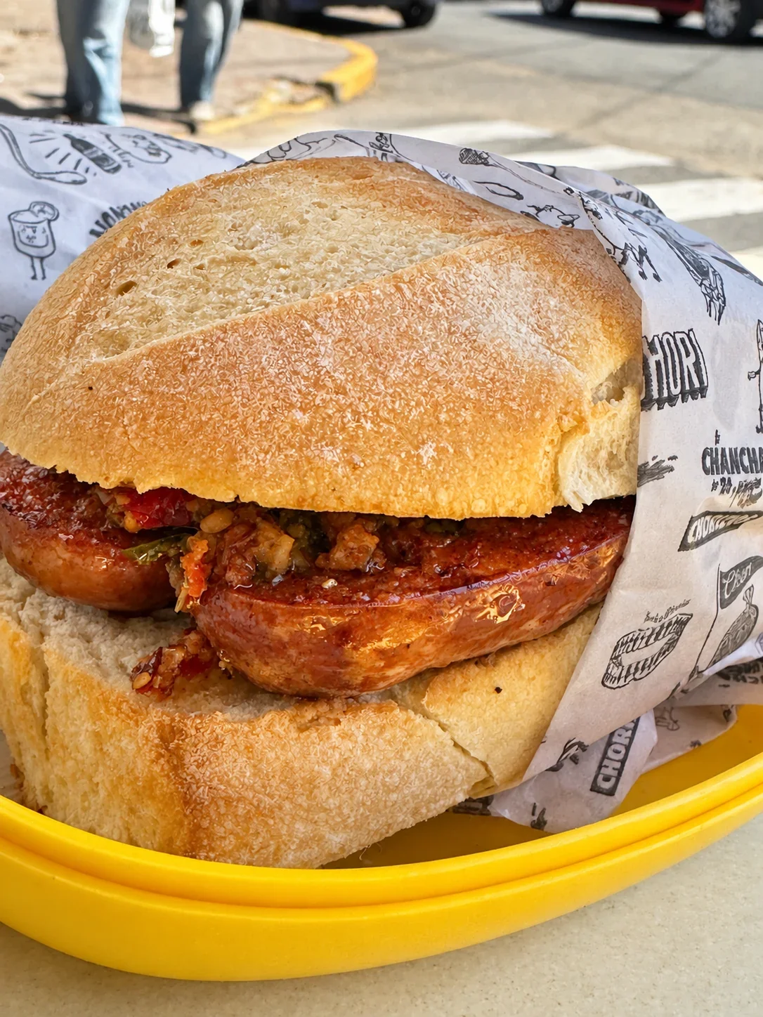 A Chori de Cancha with a split pork chorizo and chimichurri in a round roll