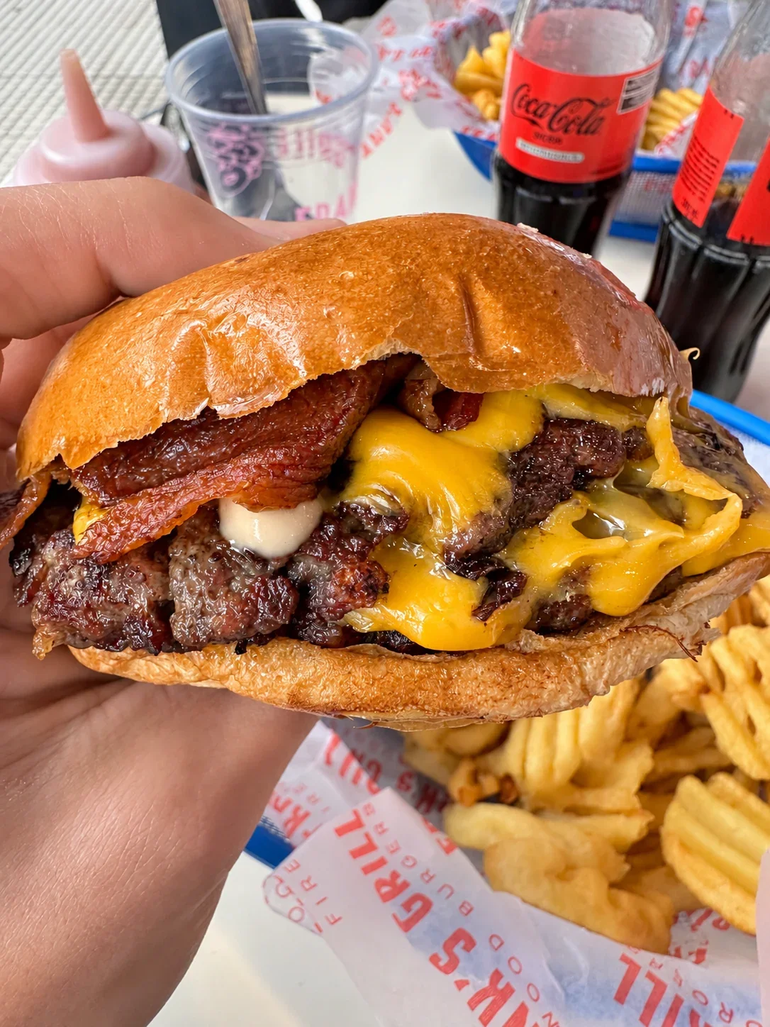 A hand holding Frank’s Grill’s double bacon cheeseburger with cheddar and sauce in a glossy bun