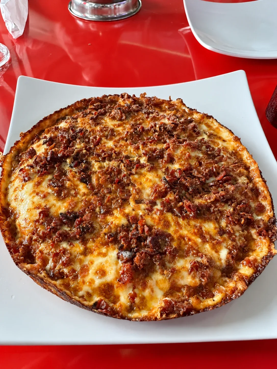 A round chorizo pizza with browned cheese to its edge on a white square plate at La Farándula
