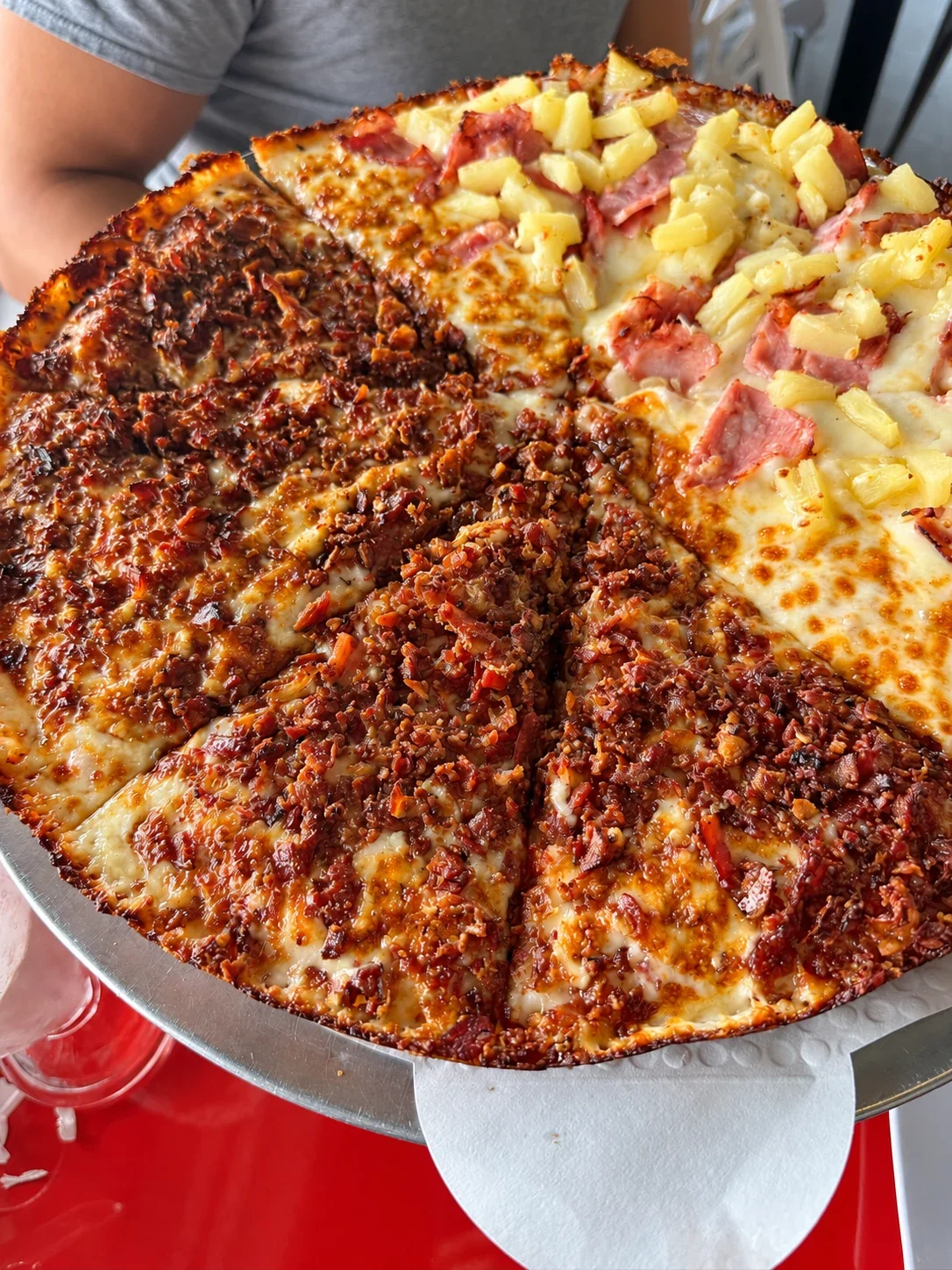 A large pizza divided between chopped chorizo and ham with pineapple on a raised tray