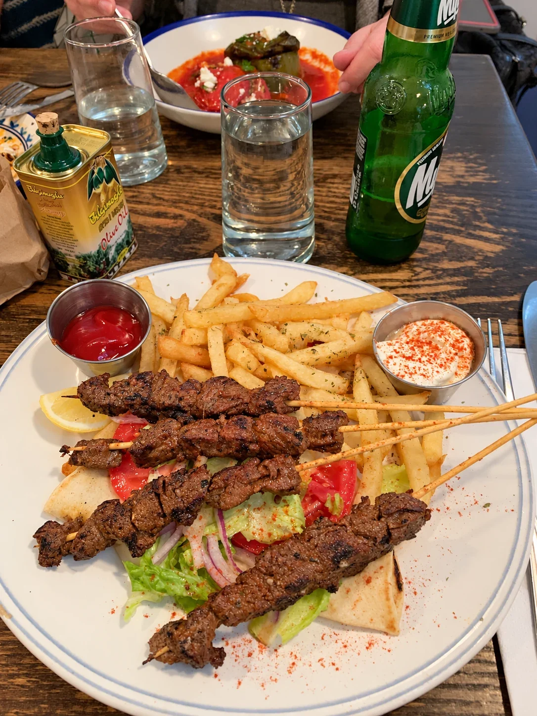 Beef souvlaki skewers with fries, pita, salad and accompaniments on a blue-rimmed plate