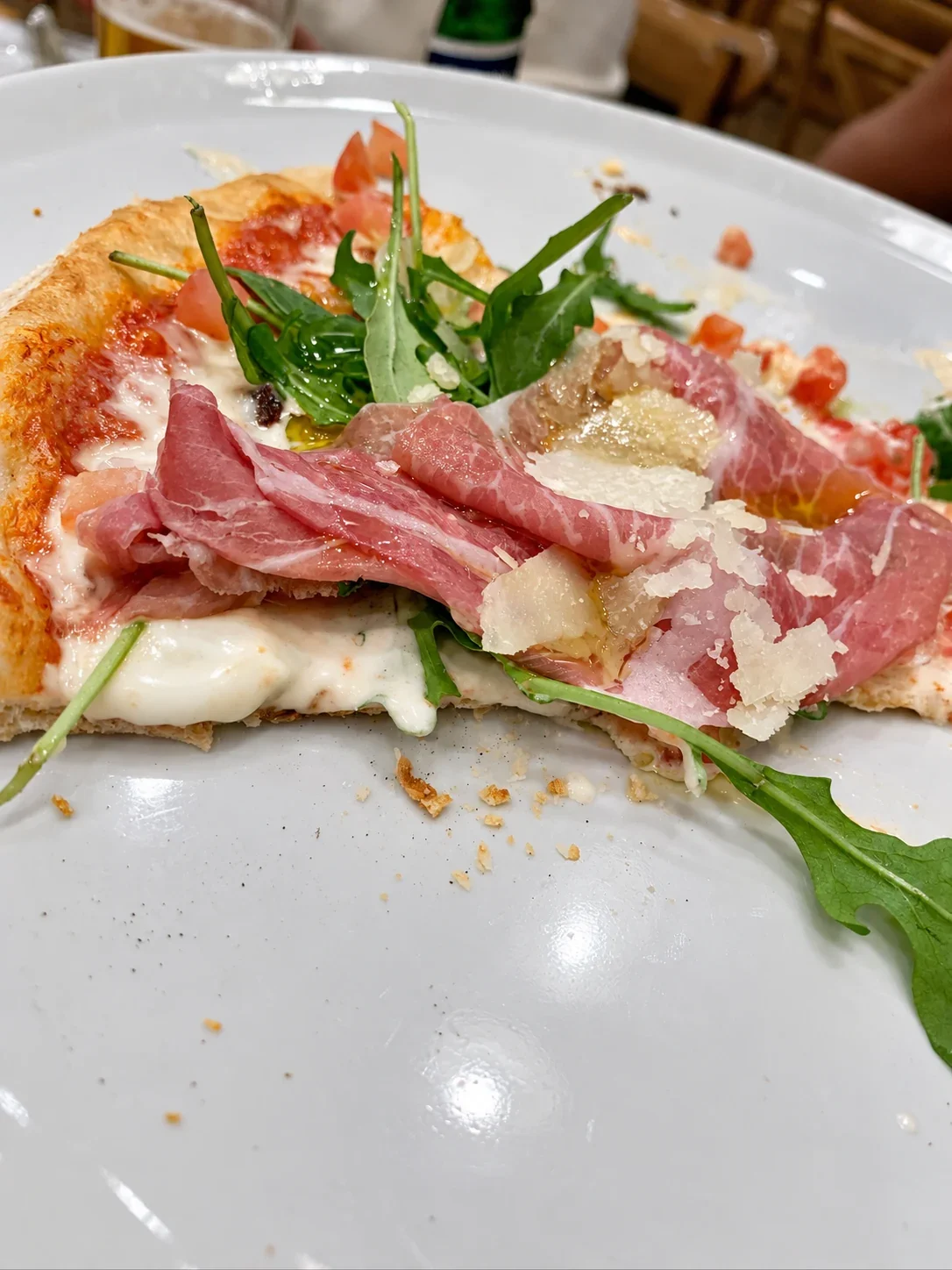 A thin slice of Marco pizza with stracciatella, prosciutto, arugula and Parmesan on a plate
