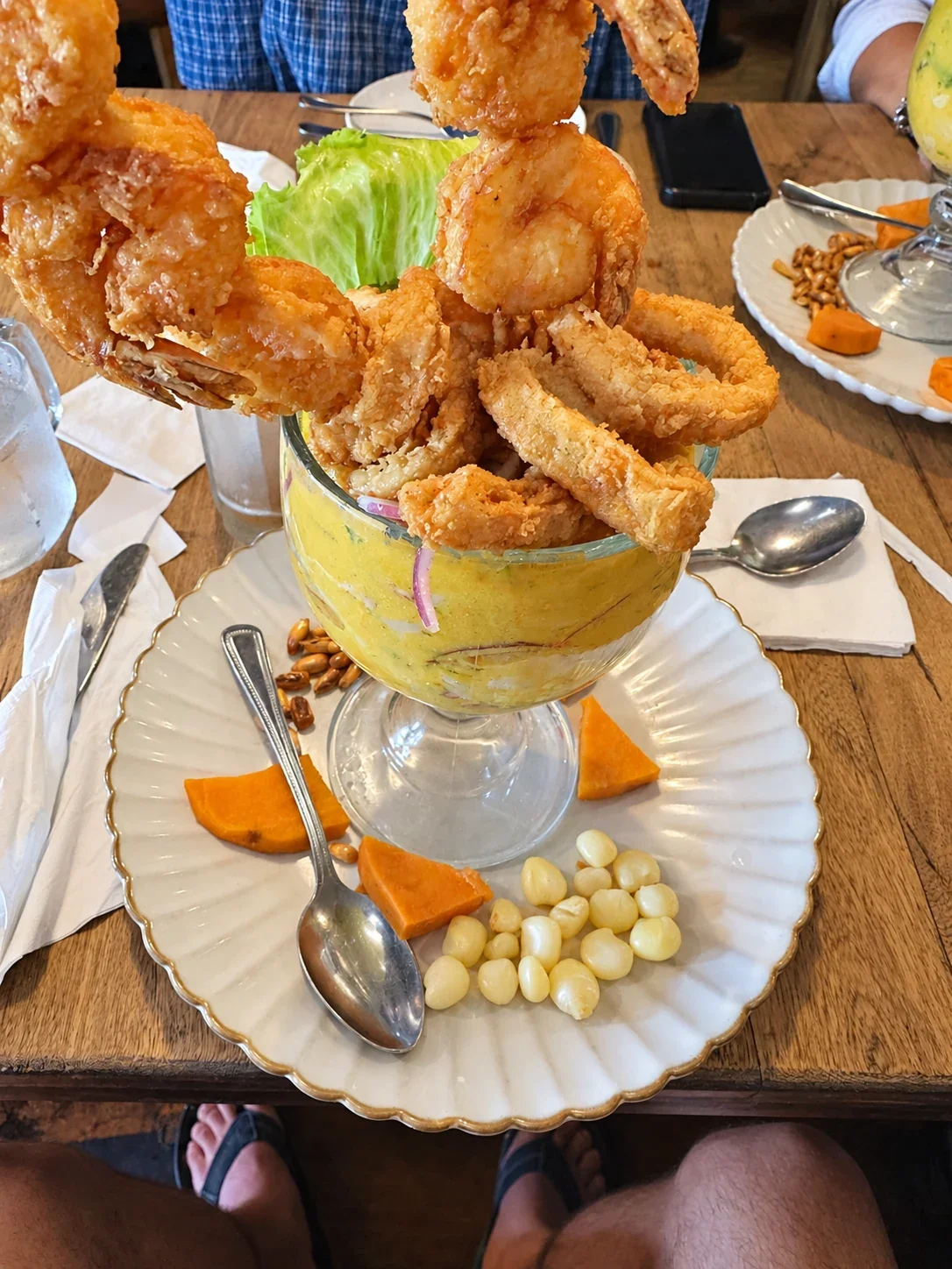A glass of ceviche topped with fried seafood and shrimp, beside corn and sweet potato at Piruw Grill
