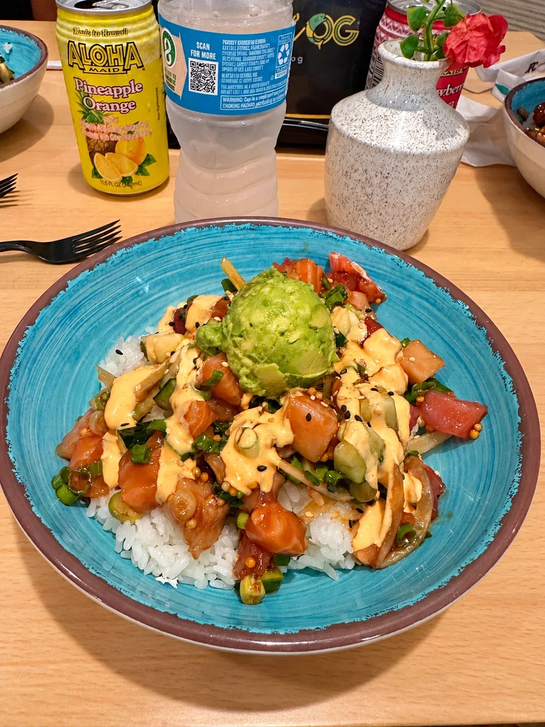 A Rainbow OG poke bowl with fish, rice, cucumber, scallions, sauce and added avocado in a turquoise bowl